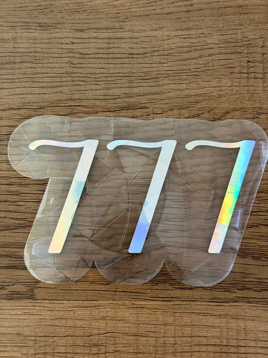 777 angel number rainbow window cling displayed on a bright window with rainbow light